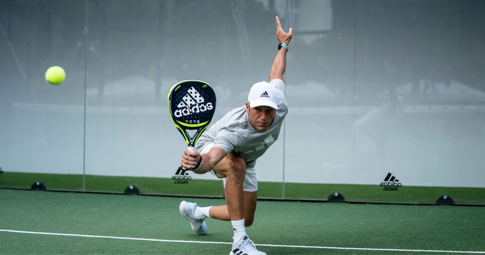 Top Game padel player stretching to reach a low shot with Adidas racket on indoor court