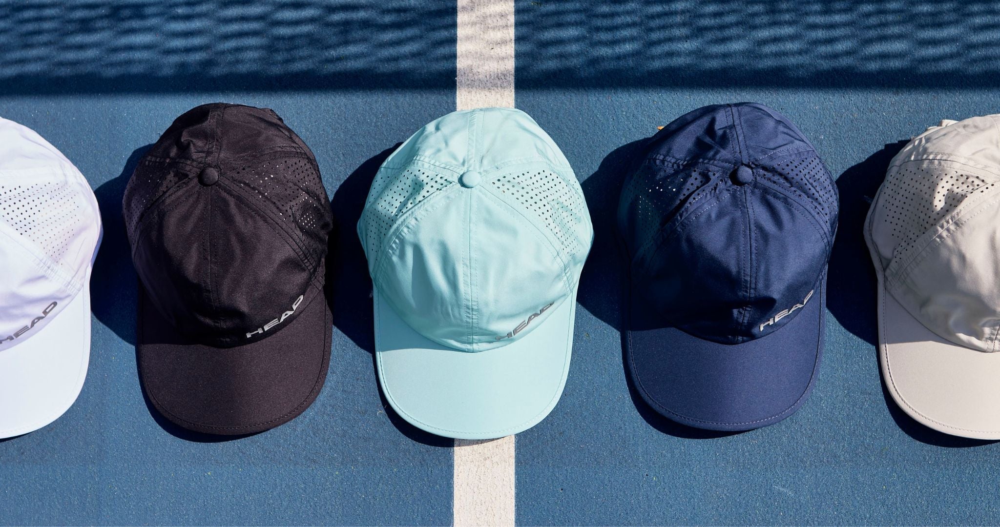 Top Game HEAD sports caps in various colors neatly lined up on blue tennis court