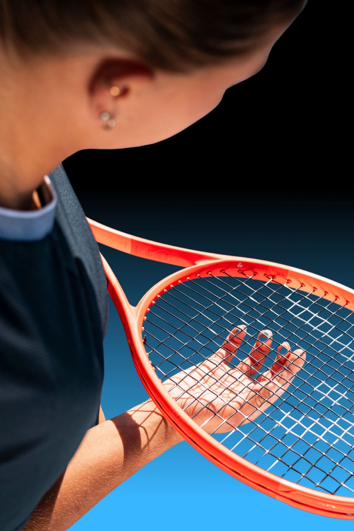 Top Game close-up of hand behind orange tennis racket strings in sunlight